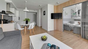Ett modernt vardagsrum med en soffa, ett matbord med stolar, en köksdel och en tv som är monterad på väggen.