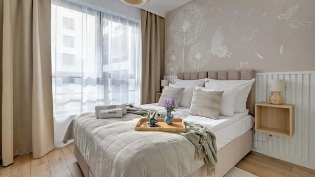 Quarto com cama, mesa de cabeceira, janela com cortinas e parede com padrões florais.