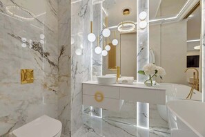 Une salle de bain moderne avec un mur en marbre, un lavabo blanc, un robinet doré et un grand miroir avec éclairage intégré.