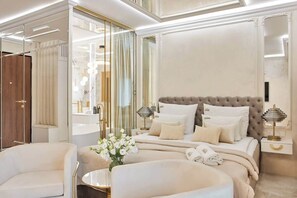 Une chambre à coucher luxueuse, dotée d’un grand lit, de tables de chevet, d’un miroir et d’une table ronde agrémentée de fleurs.