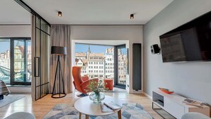 Ein modernes Wohnzimmer mit großem Fenster, Flachbildfernseher, Sofa, Couchtisch und einem Sessel.