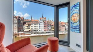 Ein modernes Zimmer mit großem Fenster, einem roten Sessel, einem kleinen Hocker und einem Gemälde.