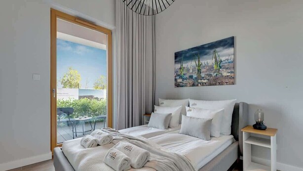Ein Schlafzimmer mit Bett, Gemälde, Nachttisch und Blick ins Freie.