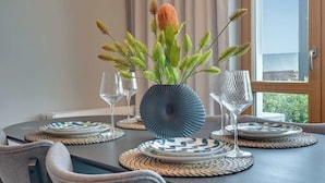 Ein Esstisch mit einer Vase voller grüner Blätter und einer einzelnen orangefarbenen Blüte, umgeben von Tellern und Gläsern.