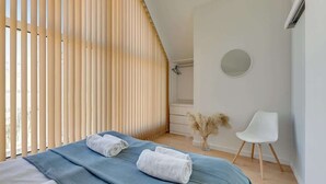 Ein Schlafzimmer mit einem Bett, einem Sessel, einem runden Spiegel und einer Vase mit Trockenblumen.