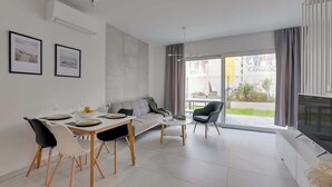 Ein modernes Wohnzimmer mit Essbereich, einer Couch, einem Fernseher und großen Fenstern.