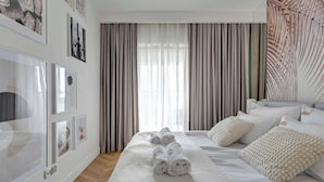 A hotel room with a large bed, a window with curtains, and artwork on the walls. - Nadmotławie Estate 129 | Riverside | Sauna & Gym (Gdańsk)