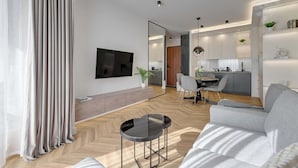 A modern living room with a sofa, a coffee table, a TV mounted on the wall, and a dining area with chairs and a table. - Nadmotławie Estate 129 | Riverside | Sauna & Gym (Gdańsk)