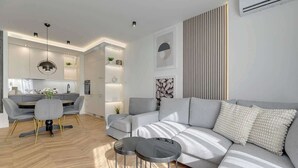 A modern living room with a grey sofa, two round tables, a dining area with a grey table and chairs, and a kitchen with built-in cabinets and pendant lighting. - Nadmotławie Estate 129 | Riverside | Sauna & Gym (Gdańsk)