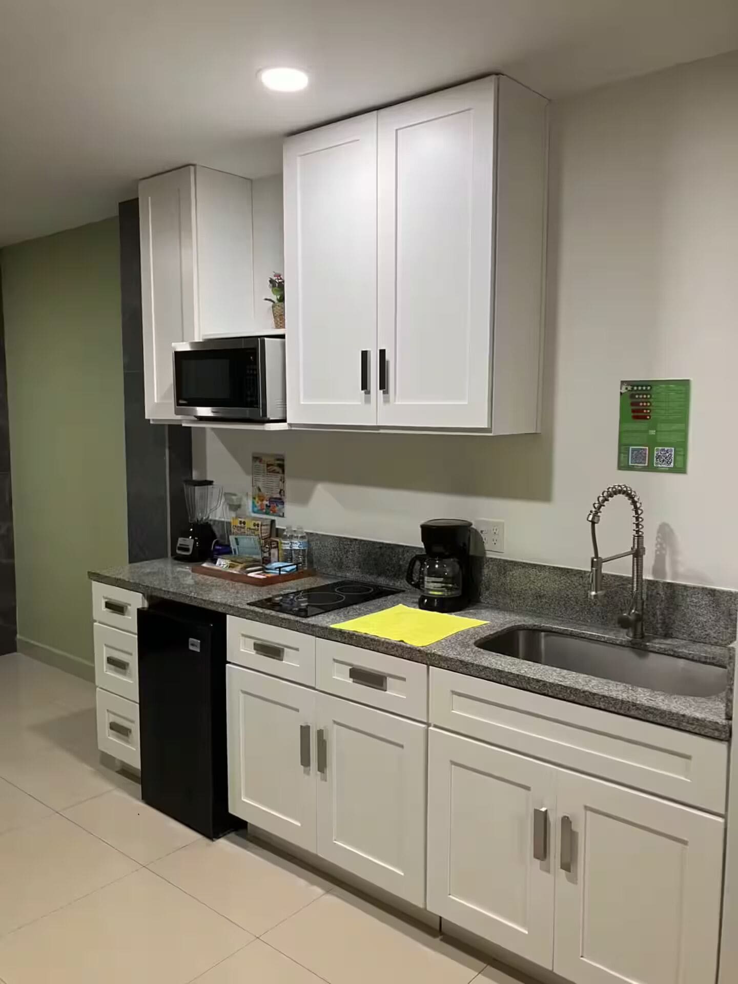 Una cocina con armarios blancos, microondas, cafetera y lavabo.