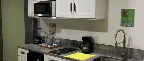 Una cocina con armarios blancos, microondas, cafetera y lavabo.