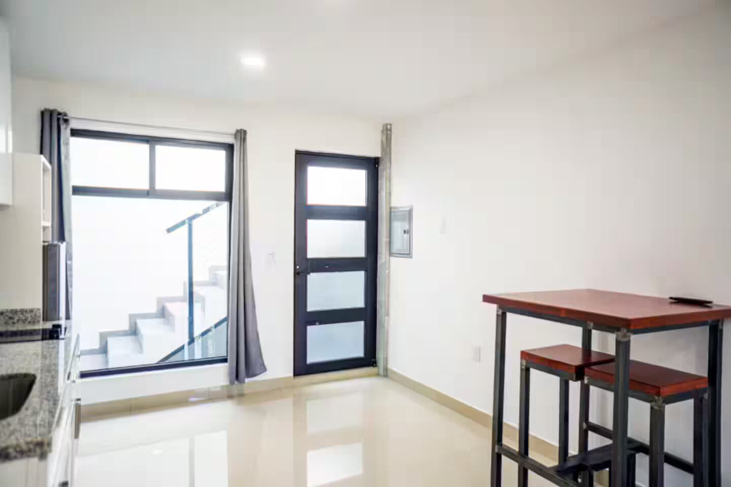 A room with a kitchen counter, a dining table, and a staircase leading to an upper floor.