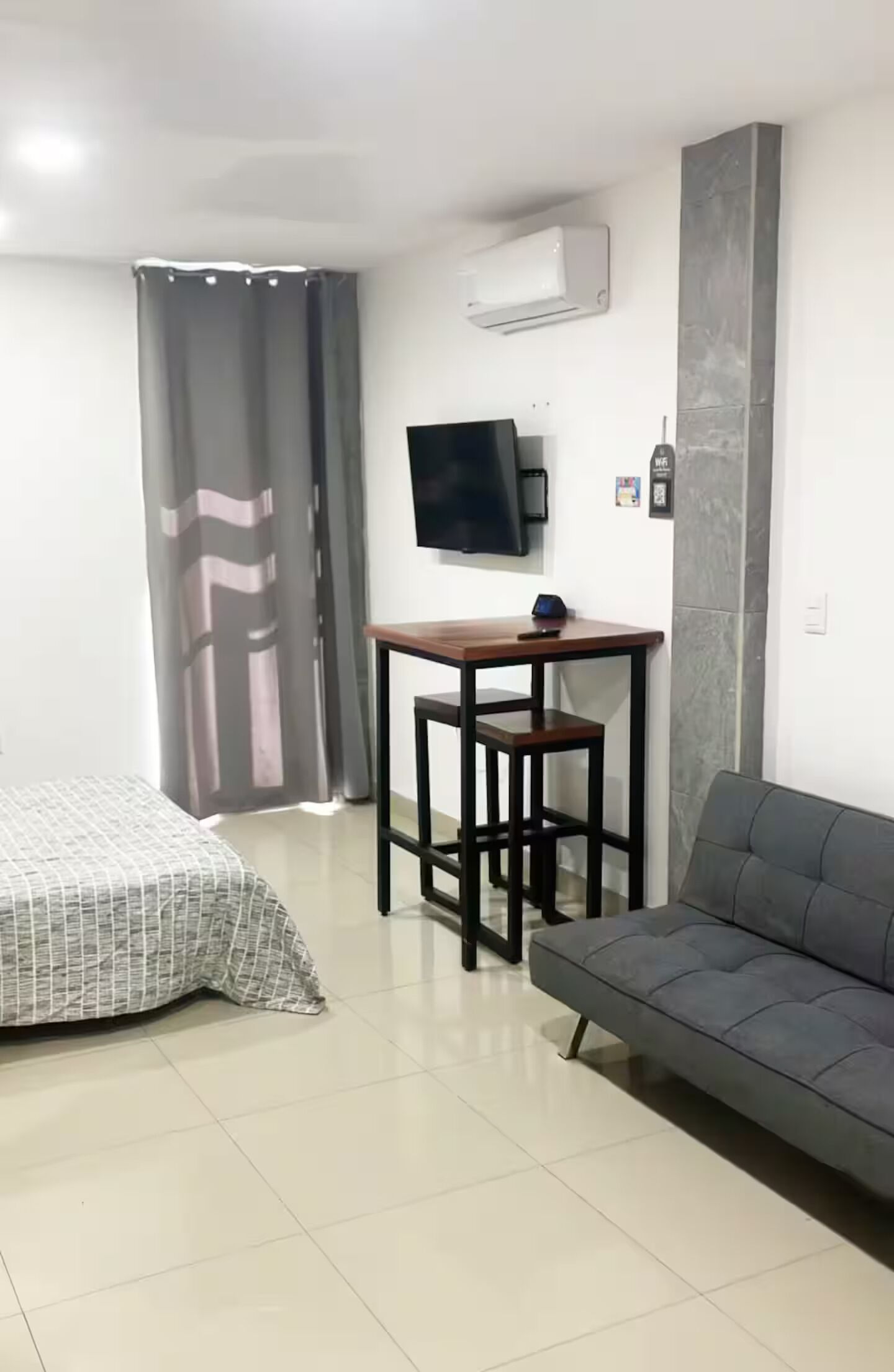 Ein Zimmer mit einem Bett, einem Schlafsofa, einem kleinen Tisch, einem Fernseher und einer Klimaanlage.