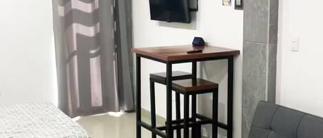 Una habitación con una cama, un sofá, una mesita, un televisor y un aire acondicionado.