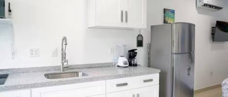 Une cuisine moderne avec des armoires blanches, un réfrigérateur en acier inoxydable, un évier encastré et une machine à café.