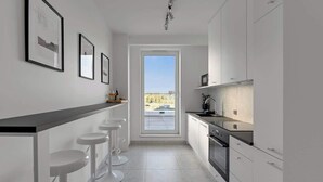 Eine moderne Küche mit weißen Schränken, einer schwarzen Arbeitsplatte und einem Fenster mit Blick auf einen Garten.