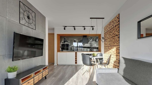 A modern living room with a flat-screen TV, a grey sofa, a dining area with a table and chairs, and a kitchen visible through an open space. - Nº 53 | Pool, SPA & Gym (Gdańsk)