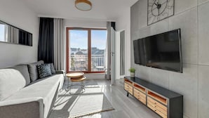 A modern living room with a sofa, TV, and a large window. - Nº 53 | Pool, SPA & Gym (Gdańsk)