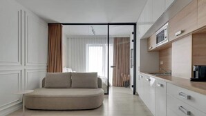 Een moderne, compacte leefruimte met een bank, kitchenette en een glazen schuifdeur naar een slaapkamer.