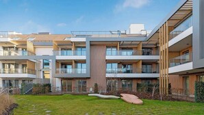 Un immeuble résidentiel moderne à plusieurs étages, doté de balcons, d’une cour intérieure et d’une pelouse bien entretenue.