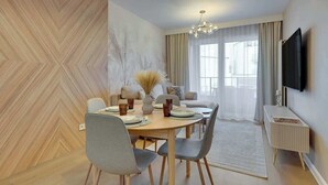 Un espace repas moderne avec une table ronde, des chaises grises, un lustre et un téléviseur fixé au mur.