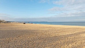 Une vaste plage de sable fin, sous un ciel dégagé et avec une ligne d’horizon lointaine.