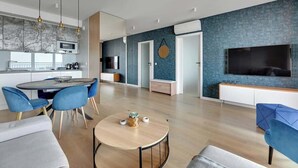 A modern living room with a round coffee table, blue chairs, a TV, and a kitchen area with a microwave. - Nº 83 with Balcony | Pool, SPA & Gym | River View (Gdańsk)