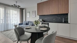 A modern kitchen with a black marble countertop, wooden cabinets, and a dining area with grey chairs and a round table. - Scala 37 with Balcony | City Center | Parking (Gdańsk)