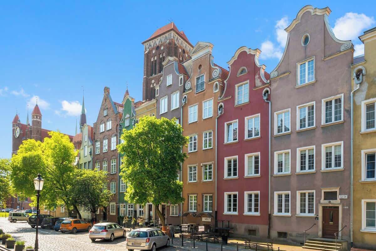 Una hilera de edificios históricos coloridos con una calle adoquinada y coches estacionados.