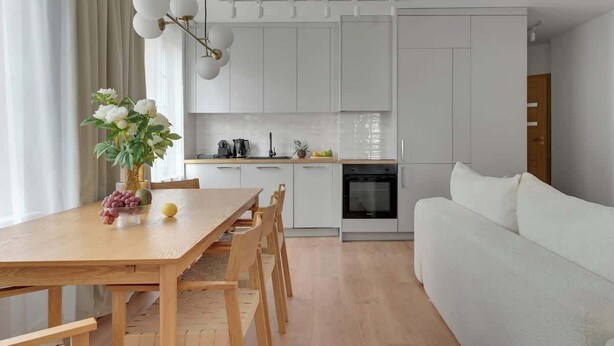 Cozinha moderna com armários brancos, uma mesa de jantar com cadeiras, um sofá branco e uma luminária pendente.