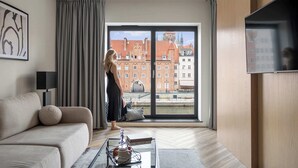 Moderni olohuone, jossa on suuri ikkuna, sohva, tarjotinalustalla varustettu sohvapöytä ja televisio.