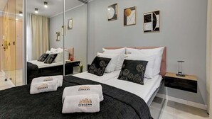 Hotellihuone, jossa on suuri peili, mustavalkoisilla tekstiileillä varustettu sänky, yöpöytä lampun kanssa ja taideteoksia seinällä.