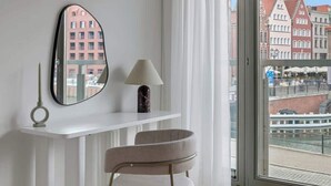 A modern room with a white desk, a chair, a mirror, and a view of buildings through a large window. - Waterlane E2 | Spa, Pool & Gym | Riverside (Gdańsk)