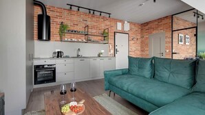 A modern kitchen with a brick wall, a green sofa, and a wooden table with fruit and wine glasses. - Granaria A607 | Best Location (Gdańsk)