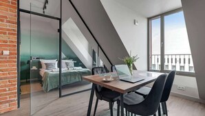 A modern loft bedroom with a glass partition, a dining area with a laptop, and a view of the city. - Granaria A607 | Best Location (Gdańsk)