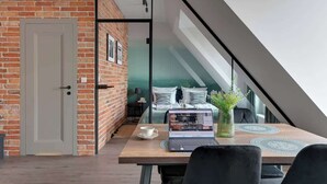 A modern room with a brick wall, a glass door leading to a bedroom, a laptop on a table, and a vase with plants. - Granaria A607 | Best Location (Gdańsk)