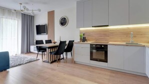 A modern kitchen with a built-in oven, a dining area with a table and chairs, and a TV mounted on the wall. - Waterlane F12 | Spa, Pool & Gym | Riverside (Gdańsk)