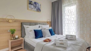 A hotel room with a bed, bedside tables, a wall-mounted artwork, and a window with curtains. - Waterlane F12 | Spa, Pool & Gym | Riverside (Gdańsk)