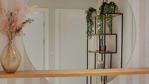 Un miroir reflétant une pièce avec une étagère en bois, un vase contenant des fleurs séchées et un présentoir à plantes en métal noir orné de verdure.