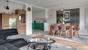 Un salon moderne avec un canapé, une table à manger et des chaises, une cuisine en arrière-plan et un élément décoratif mural.