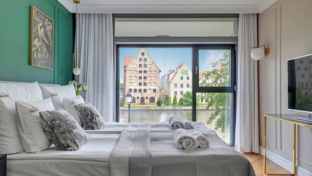 Une chambre d’hôtel avec un lit, une télévision et une vue sur les bâtiments, visible à travers une grande fenêtre.