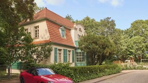 A red sports car parked in front of a large, historic building with a red-tiled roof and green shutters. - Willa Deco 5 | Lemon Apartment (Sopot)