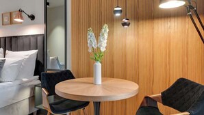 Een moderne kamer met een ronde houten tafel, twee stoelen, een witte vaas met bloemen en een houten wand met verticale lijnen.
