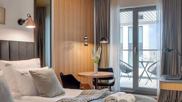 Een hotelkamer met een bed, een klein rond tafeltje met stoelen, een laptop op een bureau en een balkon met stoelen.