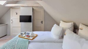 Une chambre à coucher avec un lit, des oreillers, un plateau avec une théière et des tasses, une télévision et une porte.