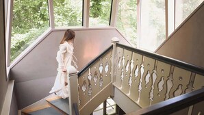 Un escalier avec une rampe, une personne qui descend, et une vue sur la verdure à l’extérieur.