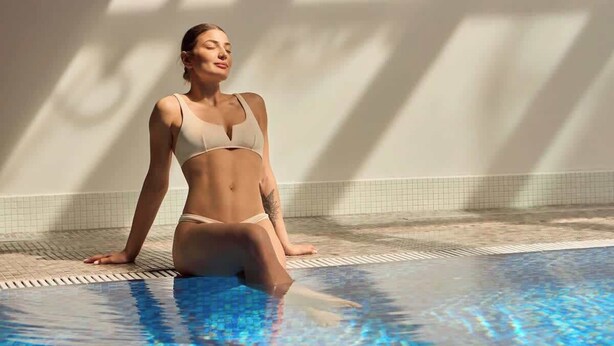 En person sitter vid en pool med kakelbeklädda väggar och ett kaklat golv.