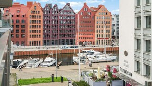 En småbåtshamn med förtöjda båtar, en modern byggnad med en röd fasad och en vit byggnad med en skylt.