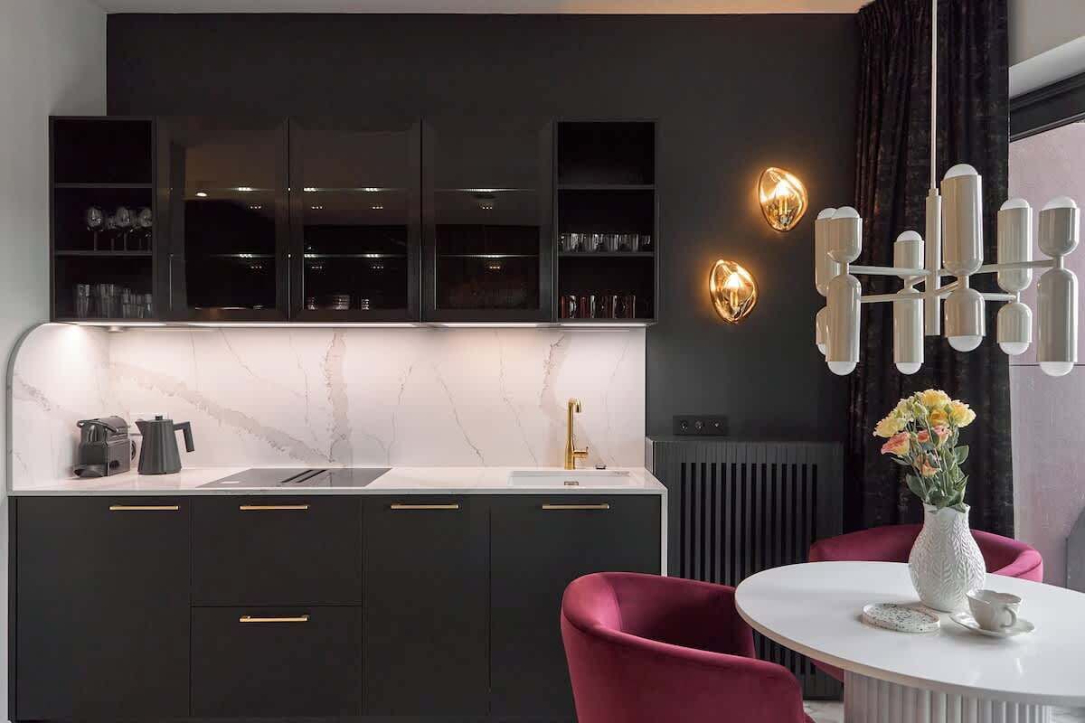 Eine moderne Küche mit dunklen Schränken, einer weißen Arbeitsplatte und einer Marmor-Spritzschutzwand. Zwei Wandleuchten und eine dekorative Leuchte sind vorhanden.