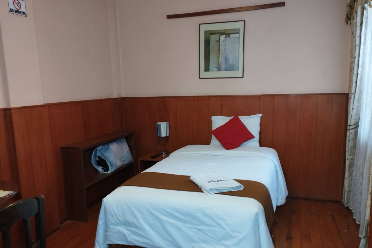 Ett hotellrum med två sängar, en TV, en sänggavel i trä, en tavla och en skylt med texten ”RÖKNING FÖRBJUDEN”.